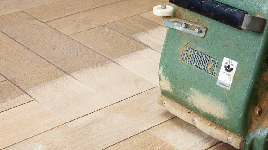 Schuurmachine RIGA schuurt een houten vloer met een schuurmachine om de vloer te renoveren.